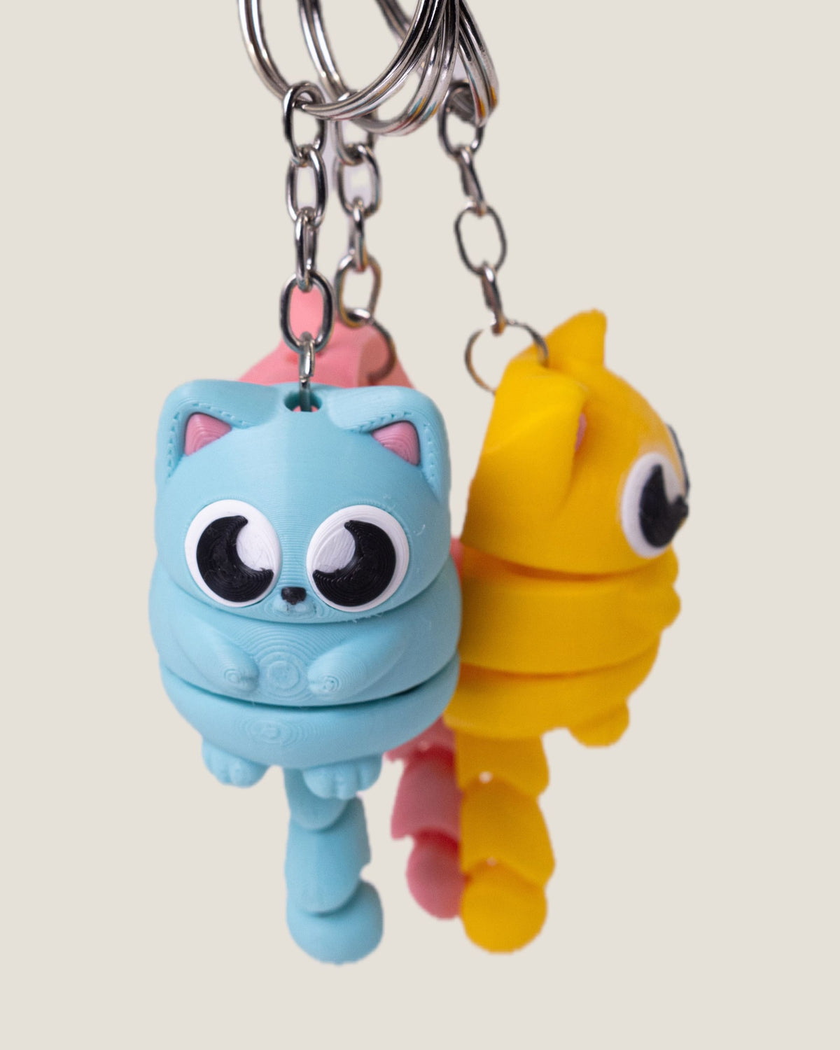 3D printed flexi cat keychains in pink, yellow and blue